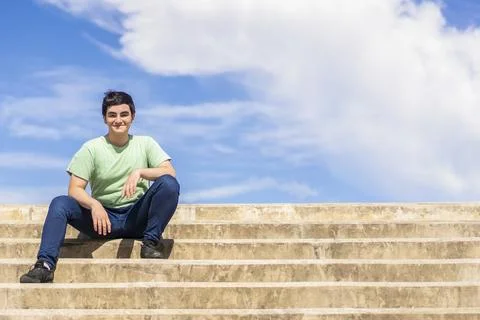 Friendly young man sitting on steps smiling against a bright blue sky Stock Photos