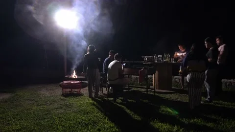 Friends and couples of men and women chatting and laughing by a campfire and gri Stockbeeldmateriaal 199523780