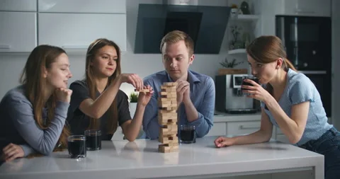 Friends are sitting in the kitchen and playing a board game of jenga. 库存影片 132858145