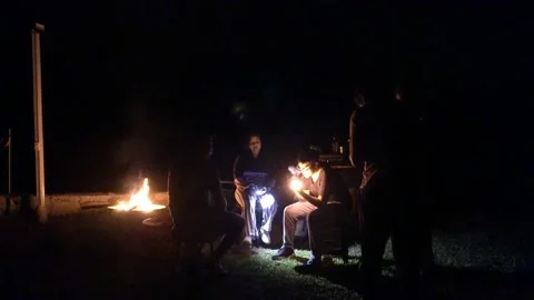 Friends around a campfire in the dark with a lantern and smoking under the stars Stock Footage 199519858