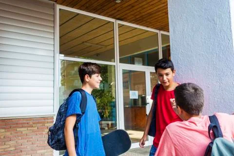 Friends with backpacks talking while standing against school building Fotos de archivo