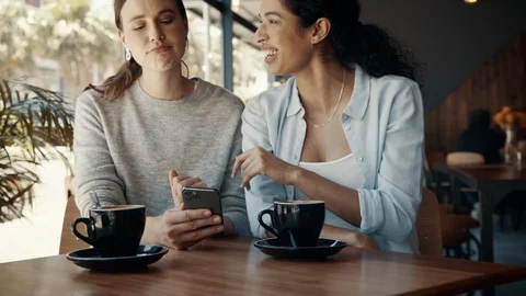 Friends at a cafe using a mobile phone and smiling Stock Footage 127820019