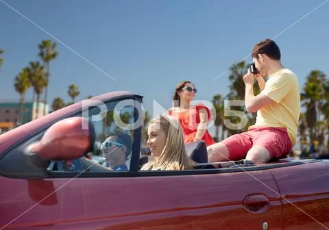 Friends with camera driving in convertible car Stock Photos