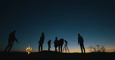 Friends with campfire looking through telescope in night Stock Footage