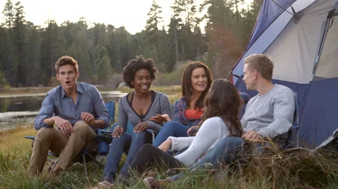 Friends on a camping trip relaxing by their tent near a lake Stock Footage