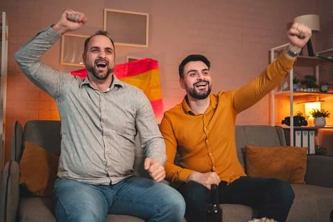 Friends celebrating joyfully while watching a thrilling match at home in a cozy Stock Photos