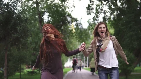 Friends cheerfully run through the summer park and hold hands. Two red Stock Footage 79092639