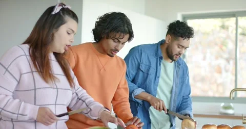 Friends chopping lettuce, tomato, bread at kitchen island raising knife and Stock Footage 335070017