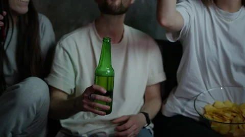 Friends clinking bottles in front of the TV. Home viewing of sports events Stock Footage 258891116