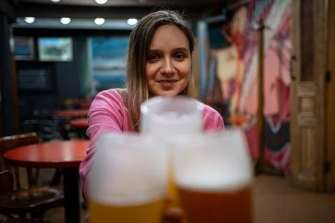 Friends clinking glasses of light beer in a pub. Smiling young woman enjoyi.. Stock-Fotos