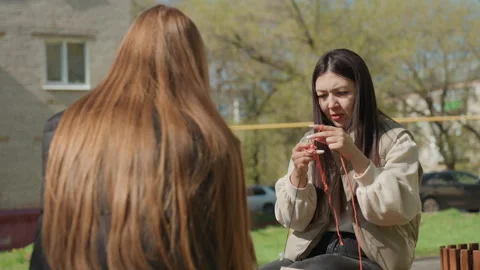 Friends collaborate on knitting project in urban park setting, women exchanging Stock Footage 330710763