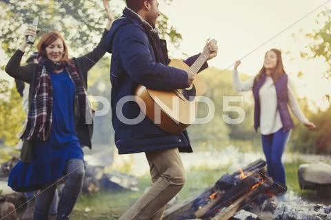 Friends dancing and playing guitar around campfire Stock Photos