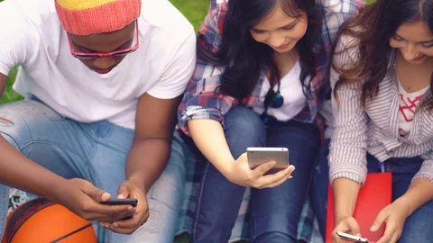 Friends of different races sitting looking at smartphones Video stock 127913445
