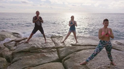 Friends doing warrior pose on rocks near seaside at dusk Stock Footage 75288265