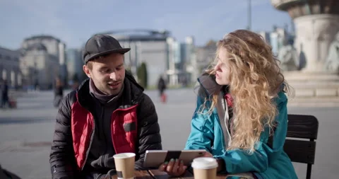 Friends Enjoying Coffee and Using Tablet at Outdoor Cafe in City Square Stock Footage 344831142