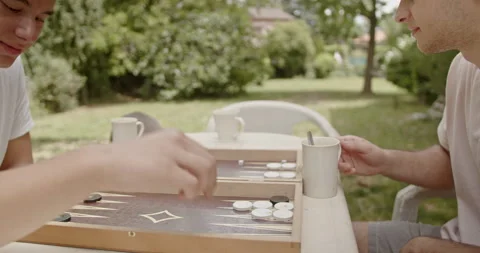 Friends enjoying a game of backgammon outdoors, with coffee cups on the table Stock Footage 281955908