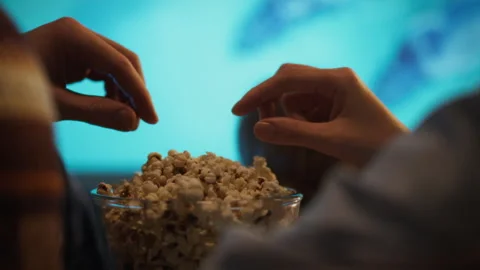 Friends enjoying popcorn while watching a movie at home during a cozy evenin Stock Footage 301374316