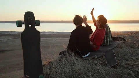 Friends give high five to each other sit at sea coast sunset rapid slow motion Stock Footage 98805405