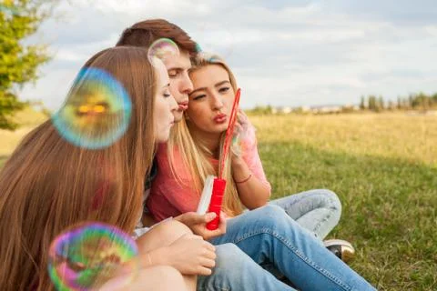 Friends having fun and blowing soap bubbles in park. Stock Photos