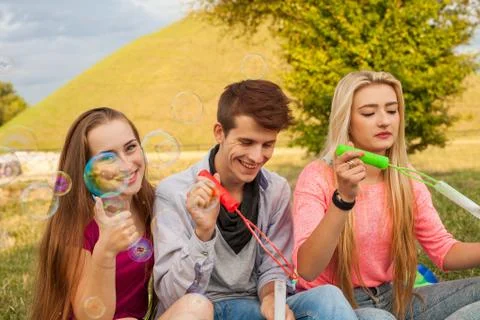 Friends having fun and blowing soap bubbles in park. Stock Photos