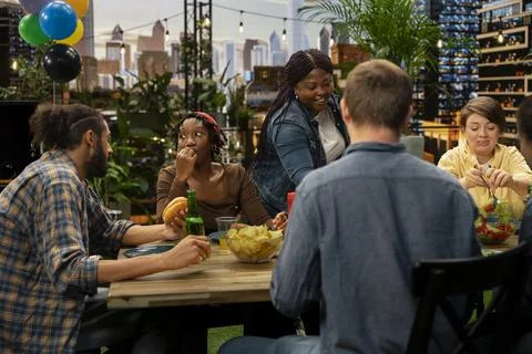 Friends having fun conversation around rooftop barbecue table Stock Photos