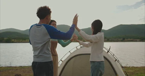 Friends high five by dome tent on grassy lakeshore at golden hour Stock-Footage 331686106