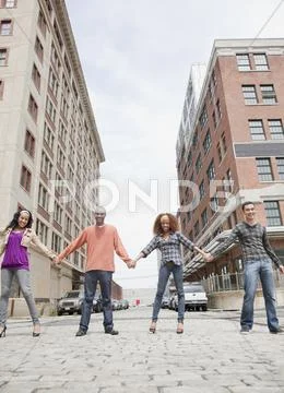 Friends holding hands and standing in a row on urban street Stock Photos