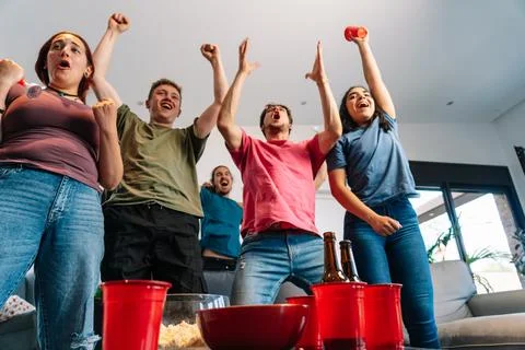 Friends jumping for joy watching e-sports on TV after their team's victory Stock Photos