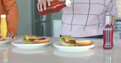 Friends at kitchen counter, flipping cap, woman squeezing ketchup onto bun and Stock Footage 340069189