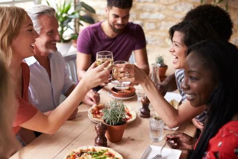 Friends laughing at a dining table in a cafe making a toast Stock Photos