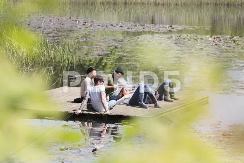 Friends laying and relaxing on sunny dock at lakeside Stock Photos