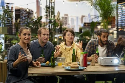 Friends lean forward beside video projector while watching sports match Stock Photos