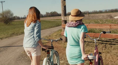 Friends Lean Their Bikes Against A Wood Fence And Walk Down Gravel Road Together Stock Footage 37401596