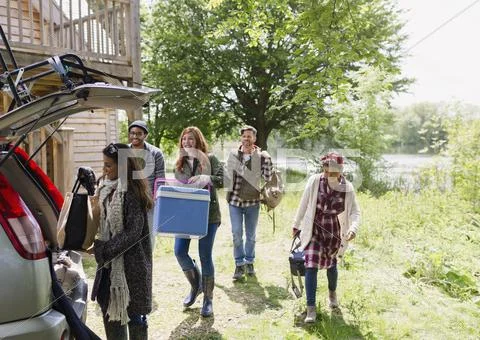 Friends loading cooler and belongings into car outside sunny cabin Stock Photos