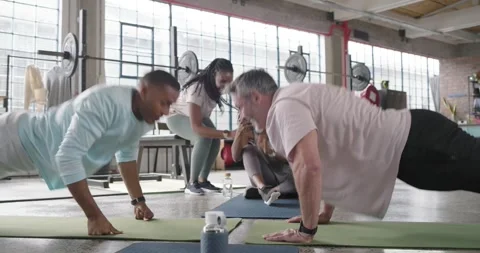 Friends in loft gym doing push-up duel on mats, men touching fists, women Stock Footage 338338326