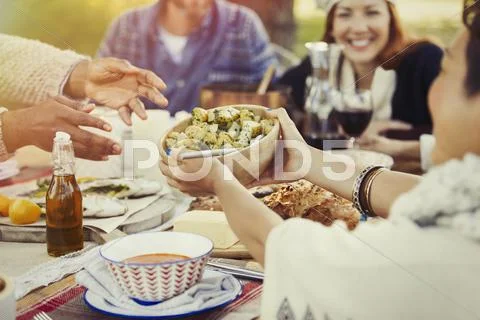 Friends passing food across patio lunch table Stock Photos