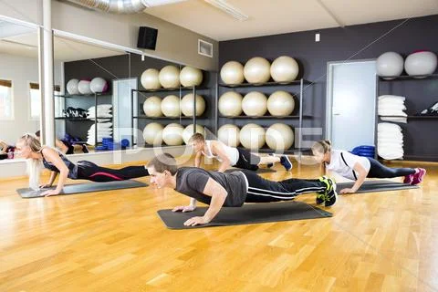 Friends Performing Pushups On Mat In Gym Stock Photos