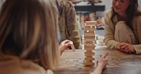 Friends playing block tower game. Tilt up view of young woman removing block Video stock 172553550