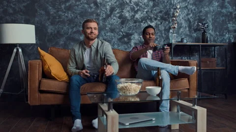 Friends Playing Console Games at Home Drinking Beer. Friends at Couch. Gamers at Stock Footage 217867531