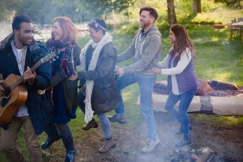 Friends playing guitar dancing in conga line at campsite Stock Photos