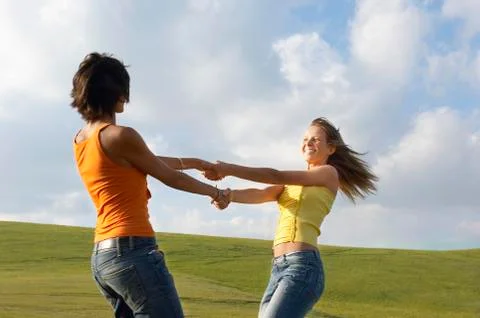 Friends Playing While Holding Hands Against Cloudy Sky Stock Photos