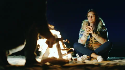 Friends relaxing around the campfire. Woman drinking tea from a cup, a man Stock Footage