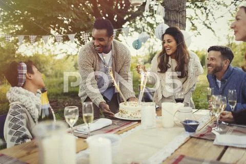 Friends serving birthday cake at party at patio table Stock Photos
