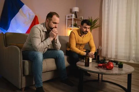 Friends share a tense moment while watching an event in a cozy living room Stock Photos