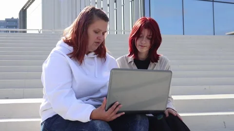 Friends sharing ideas while working on a laptop outdoors in vibrant city setting Video stock 295275934