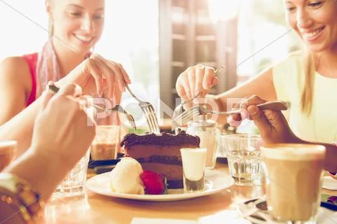 Friends Sharing Slice Of Chocolate Cake In Restaurant