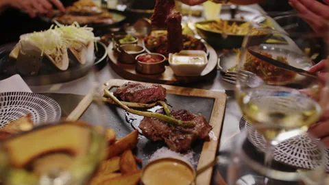 Friends Sharing Steak and Wine at a Restaurant Dinner Table with Assorted Dishes Stock Footage 342285870