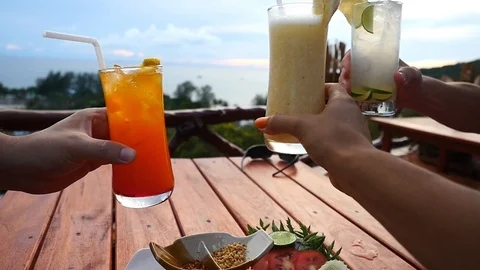 Friends sit in a cafe among mountains overlooking the sea clink tasty cocktails Видео 101286155