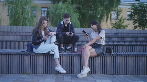 Friends sit on the steps, look at their phones, there are bottles nearby. Stockbeeldmateriaal 202311933