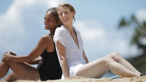 Friends sitting back to back on a beach. 스톡 동영상 88370059